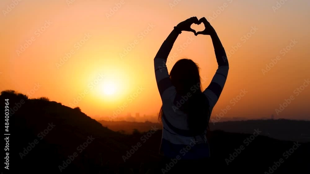 Sunset silhouette of beautiful Indian woman making heat shape with hands in background of orange sky. Concept of love and happiness. Female enjoying evening at mountain top Sunset silhouette of beautiful Indian woman making heat shape with hands in background of orange sky. Concept of love and happiness. Female enjoying evening at mountain top