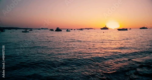 Famous, beautiful beach at sunset with calm sea near Café del Mar, in summer very popular, sandy coast have a fantastic view of island of ibiza. Moored vessels on bay. Ibiza Island, Balearic Islands photo