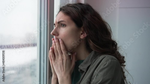 Brunette woman with curly hairstyle looks in shock out of window at crime scene at police flashing red lights with raindrops on glass photo