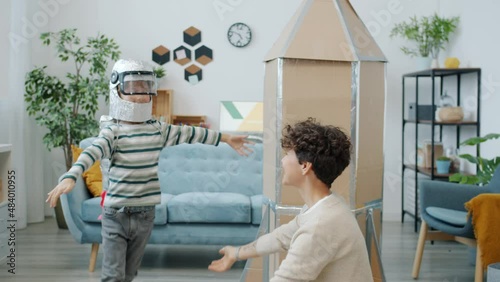 Cute little boy wearing space suit running around rocket and kissing mother at home. Futuristic game and enjoyable activity concept.