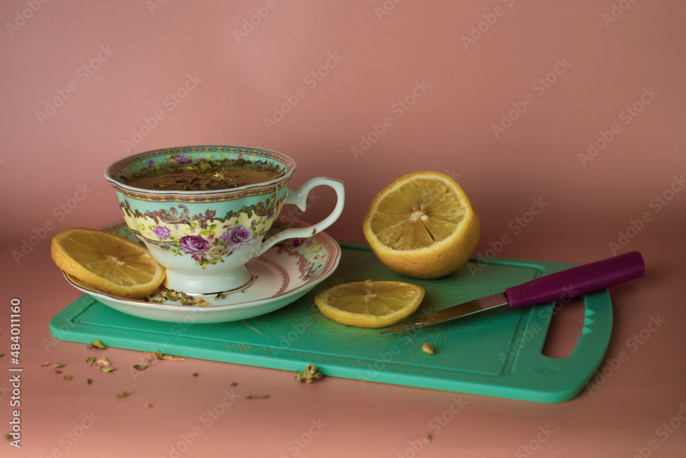 turquoise cup with flowers with green tea with lemon on a blue cutting board on a pink background