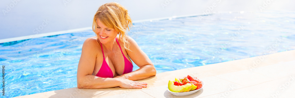 Naklejka premium Woman in bikini standing at poolside next to plate of fresh fruit