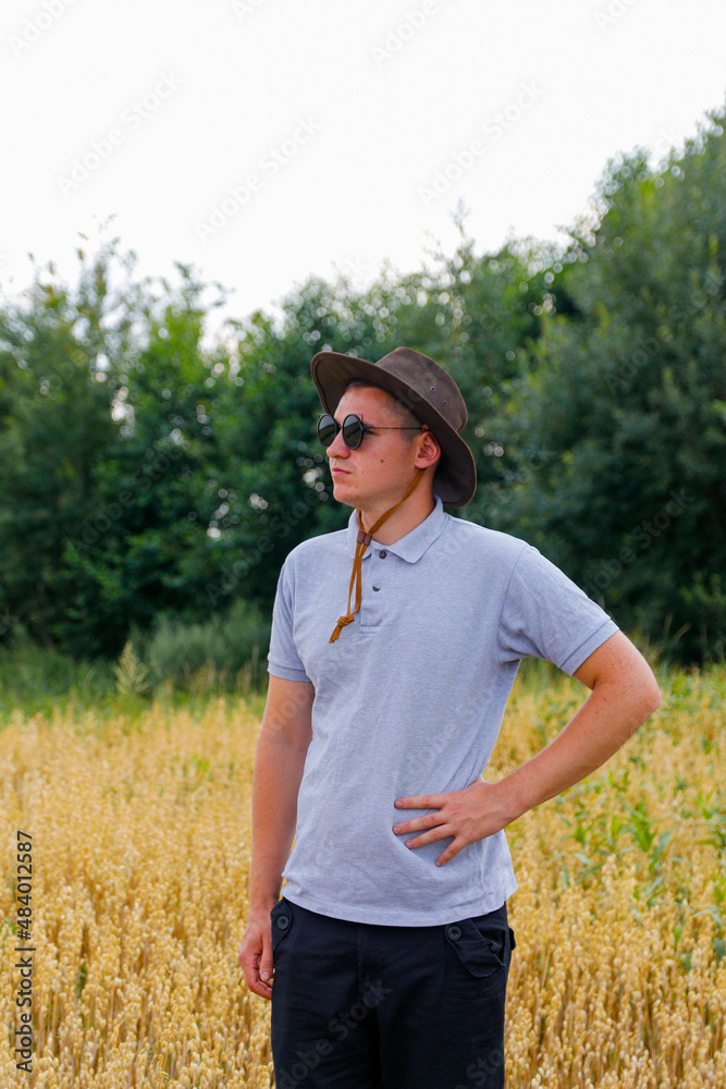 Crop and harvest. Portrait of farmer standing in gold wheat field with blue sky in background. Young man wearing sunglasses and cowboy hat in a field examining wheat crop. Oats grain production Crop and harvest. Portrait of farmer standing in gold wheat field with blue sky in background. Young man wearing sunglasses and cowboy hat in a field examining wheat crop. Oats grain production