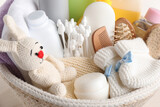 Wicker basket full of different baby cosmetic products, bathing accessories and toy on table, closeup