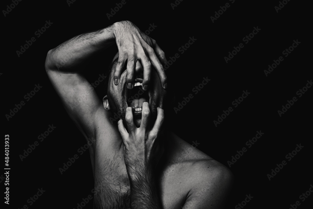 Obraz premium Portret mężczyzny w stylu horroru. Czarno-biały portret mężczyzny na czarnym tle. Mężczyzna otwiera szczękę dłońmi
