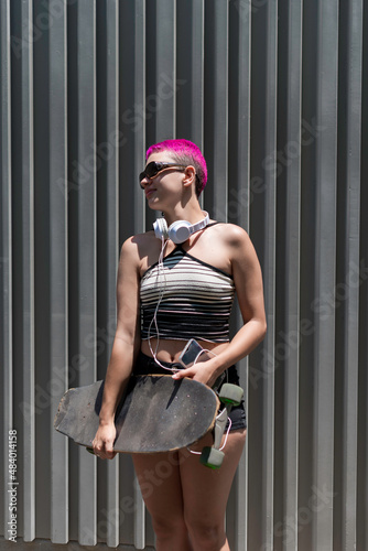 Young woman with photo sensitivity wearing sunglasses and holding the skateboard in her hand.