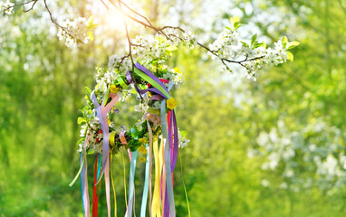 Spring flower wreath with colorful ribbons in garden, green natural background. floral decor. Symbol of Beltane, Wiccan Celtic Holiday beginning of summer. pagan witch traditions and rituals