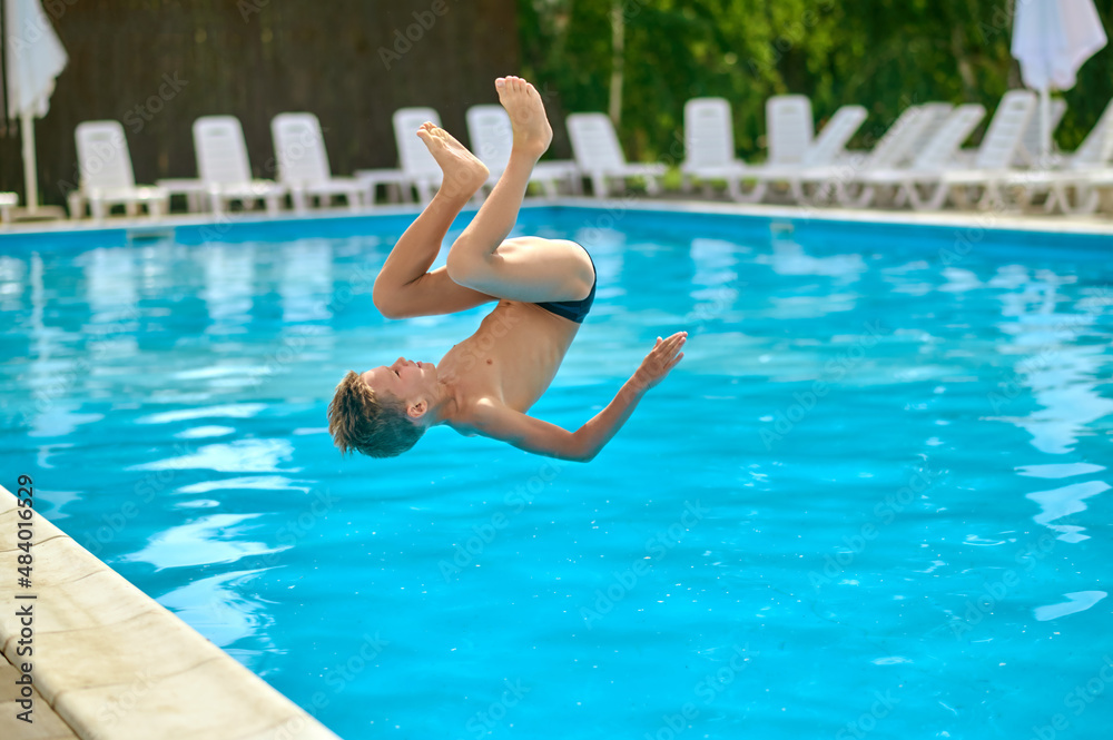 Boy in air upside down above pool water