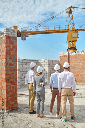 Four people in protective helmets inspecting the building area