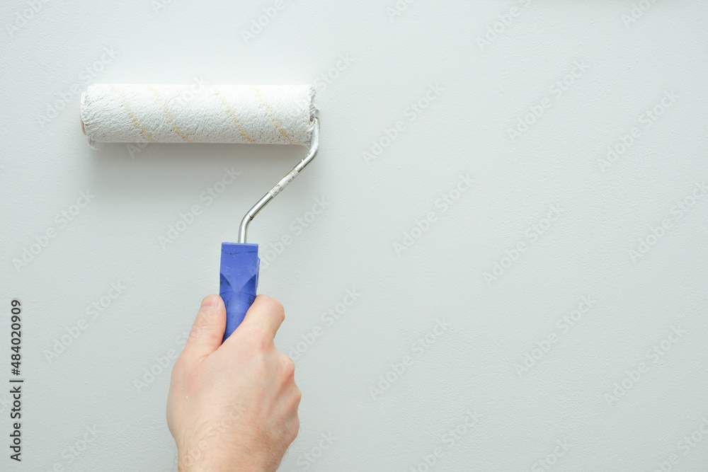 Painting works. A man paints a light wall with a paint roller. Close-up on  a hand with a tool. Construction worker, tool, apartment renovation. foto  de Stock | Adobe Stock