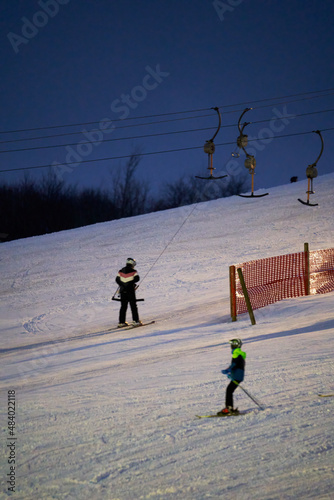 Ski drag lift in operation at night with lighting. Winter athletes on the slopes in the snow. Long exposure, blurred. photo
