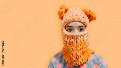 A teenage girl is dressed in a balaclava with bear ears, knitted with her own hands using alize puffy threads. New hat style. photo