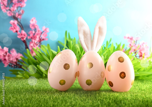 Easter eggs in grass against blurred blue blooming background. Spring holidays concept