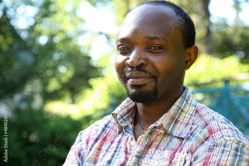 Young african man, portrait in his outdoor shirt, looking into the camera, outdoor in park, sunny atmosphere