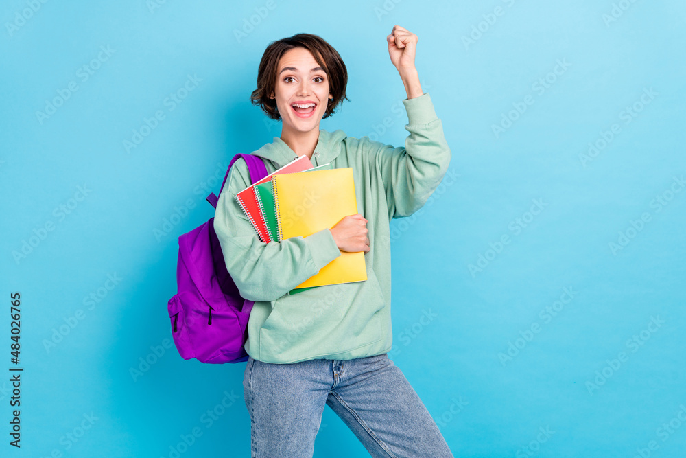 Photo of shiny lucky lady dressed green pullover backpack rising fists holding copybooks isolated blue color background