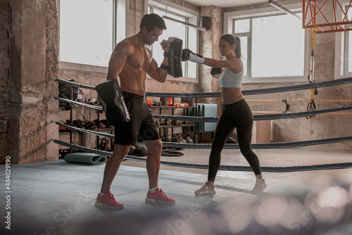 Young lady practicing boxing with strong man on the ring holding boxing paws