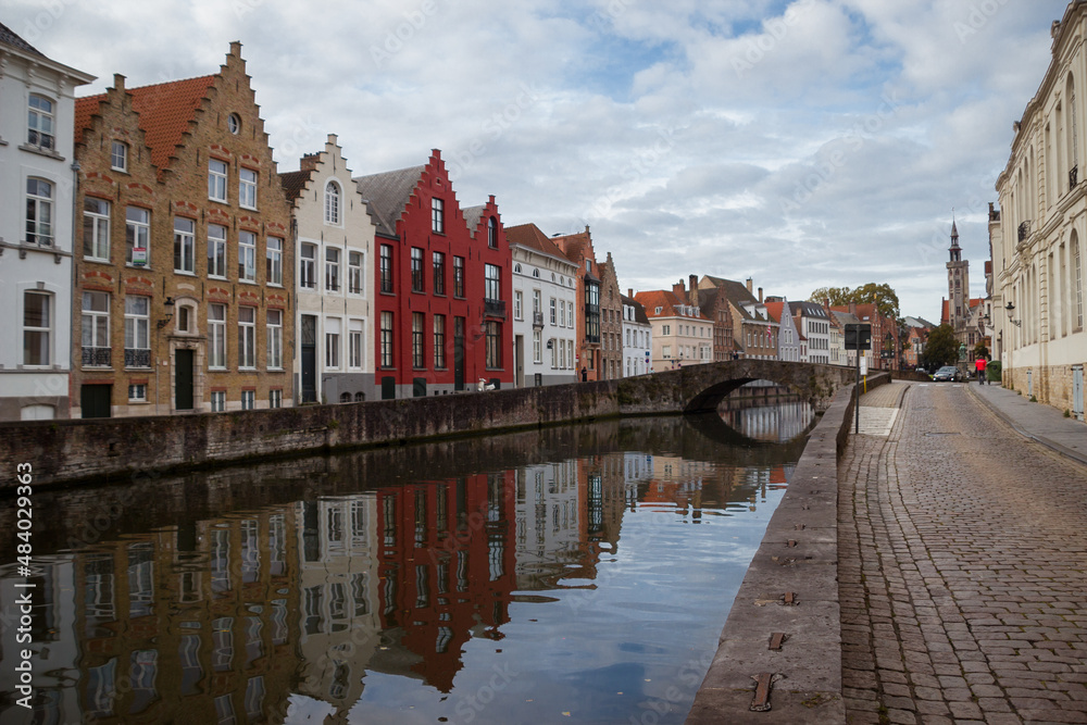 Naklejka premium Imagen de casitas de colores reflejadas en las aguas de los Canales de brujas Belgica con un vuelo azul con nubes y un puente de piedra al fondo haciendo viaje de turismo por europa
