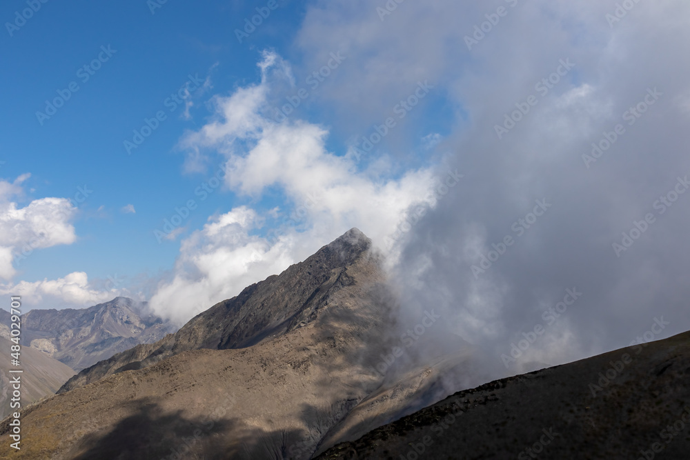 Clouds accumulating around the sharp mountain peaks of the Chaukhi Pass in the Greater Caucasus Mountain Range in Georgia, Kazbegi Region. Mountain Ridges, Hiking. Georgian Dolomites. Cloudscape