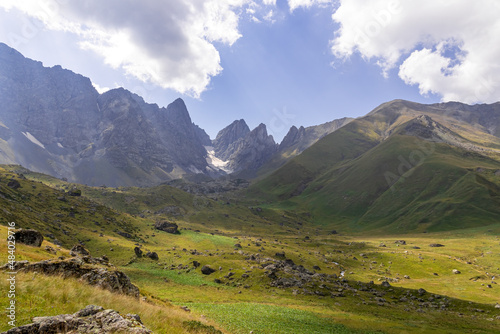 A panoramic view on the sharp mountain peaks of the Chaukhi massif in the Greater Caucasus Mountain Range in Georgia  Kazbegi Region. A hiking trail on a green alpine pasture. Georgian Dolomites.