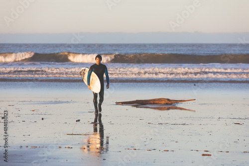 Photography Young caucasian man walking on the beach with a surfboard.