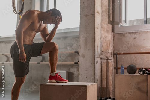 Young strong muscular male resting after exhausting workout with wooden box in crossfit gym