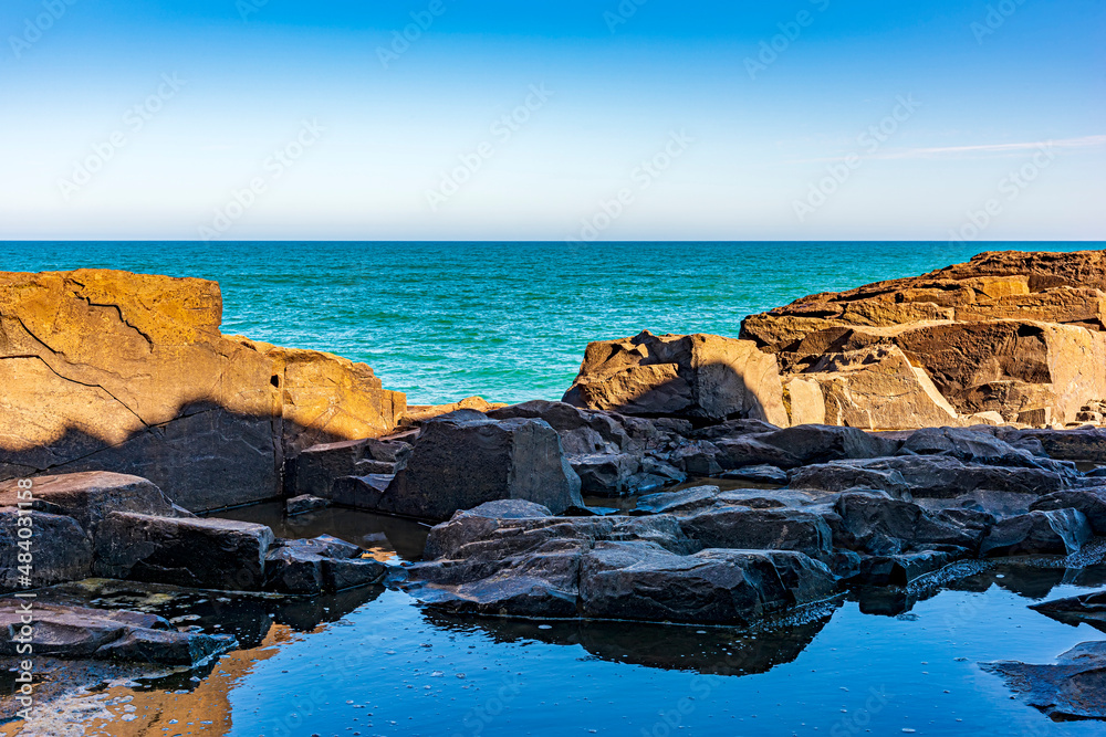 Rock formation in front of the sea and the horizon in a blue sky afternoon in Torres city, Rio Grande do Sul, Brazil