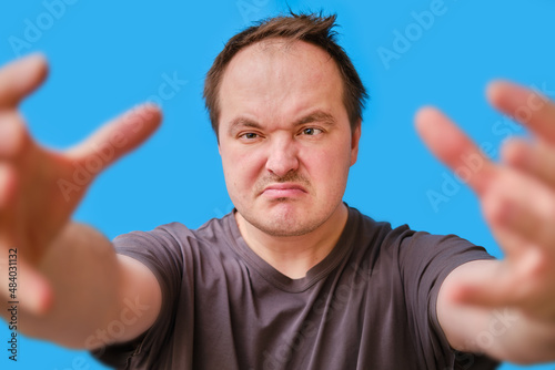 Portrait of a disheveled-looking adult man pulling his arms forward, blue studio background