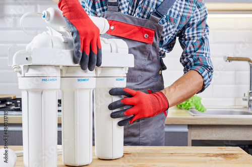 Plumber installs or change water filter. Replacement aqua filter. Repairman installing water filter cartridges in kitchen. Installation of reverse osmosis water purification system.