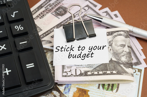 On a brown background lies a calculator and dollars on a clip with an inscription on paper - Stick to your budget photo