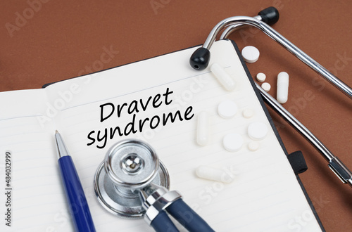 On a brown surface lie pills, a pen, a stethoscope and a notebook with the inscription - Dravet syndrome photo