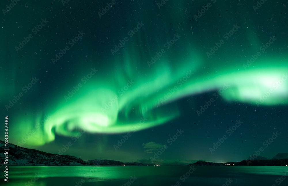 Whirling aurora borealis in nightsky reflecting on sea and land