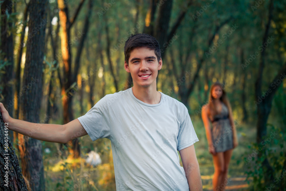 A young guy is waiting for a beautiful girl standing by a tree. A couple on a date in nature. A man with dark hair in a city park A young guy is waiting for a beautiful girl standing by a tree. A couple on a date in nature. A man with dark hair in a city park
