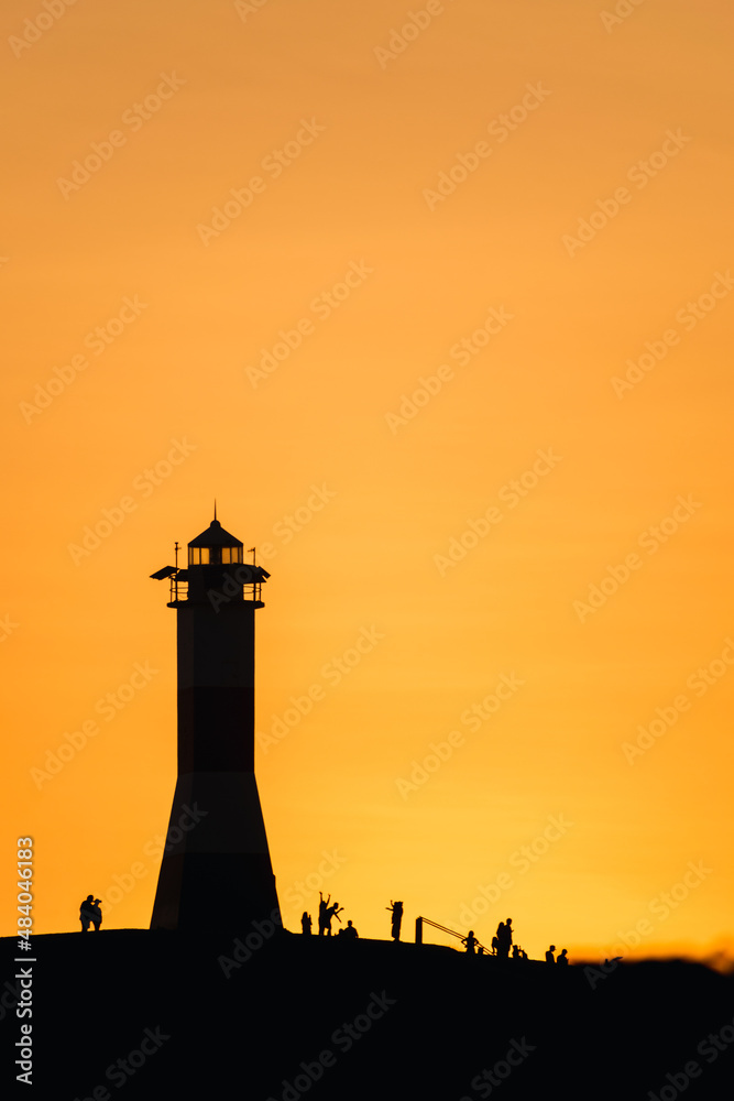 silhouette of a lighthouse with people at sunset with an orange sky on the shores of mancora beach in piura