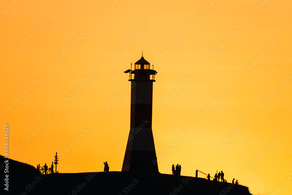 silhouette of a lighthouse with people at sunset with an orange sky on the shores of mancora beach in piura