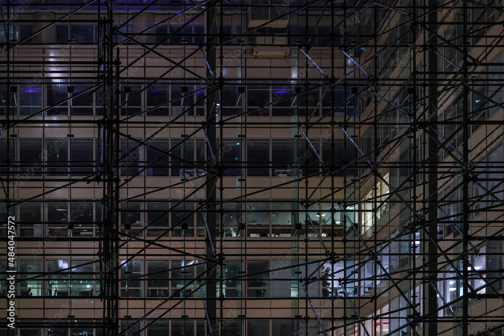 Iron scaffolding construction around steel and glass modern office building in night