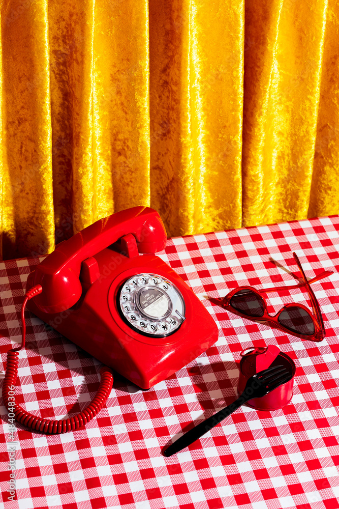 Red retro telephone and old fashion sunglasses placed on table