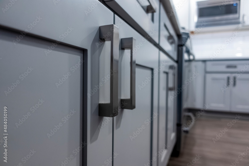 Low angle view of gray kitchen cabinet door handles inside a large, beautiful kitchen with finished, hardwood floors Low angle view of gray kitchen cabinet door handles inside a large, beautiful kitchen with finished, hardwood floors