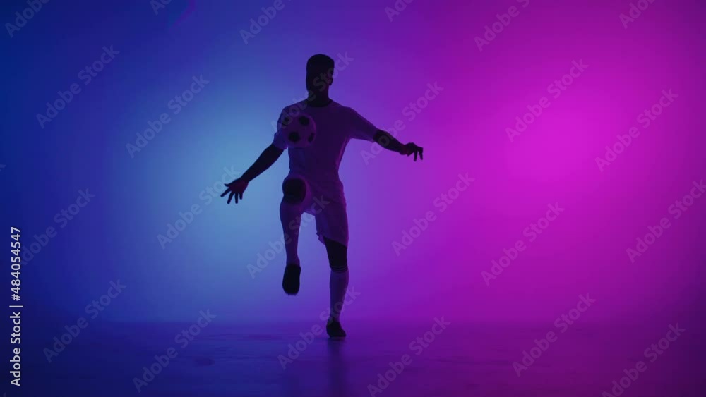 Black man a player juggles football ball in a dark studio with neon lights on the floor and red and blue lighting effects in slow motion. African professional football soccer player Black man a player juggles football ball in a dark studio with neon lights on the floor and red and blue lighting effects in slow motion. African professional football soccer player