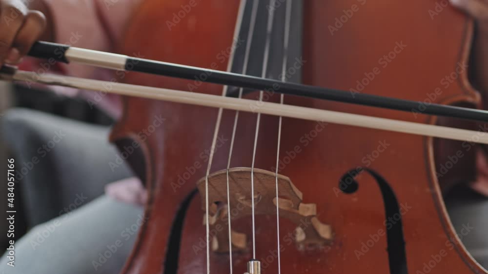 Close-up of cropped unrecognizable musician playing double bass with bow sitting indoors