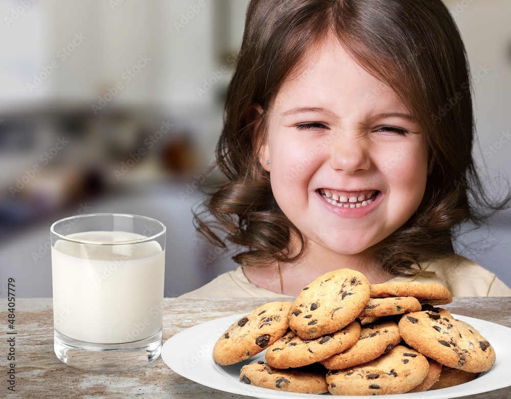 Portrait of sad girl holding glass of milk and dreaming, sitting on dinning table in kitchen interior Portrait of sad girl holding glass of milk and dreaming, sitting on dinning table in kitchen interior