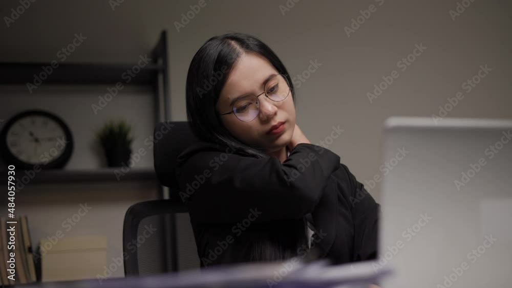 Young businesswoman works late at night in a dimly lit room. she tired and stressed needs rest. She has shoulder neck and back pain. Working hard and overtime too much going to symptom office syndrome Young businesswoman works late at night in a dimly lit room. she tired and stressed needs rest. She has shoulder neck and back pain. Working hard and overtime too much going to symptom office syndrome