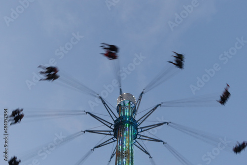 Unidentified people riding on spinning swing carousel in amusement park. Entertainment concept - High spinning swing carousel against blue sky. Motion blur photo