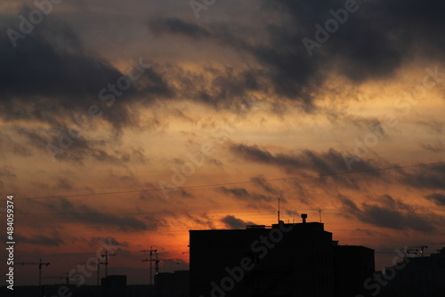 urban house and building cranes against the backdrop of a sunset sky with clouds