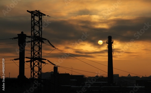 the sun among the clouds surrounded by a gloomy industrial landscape in black and orange colors