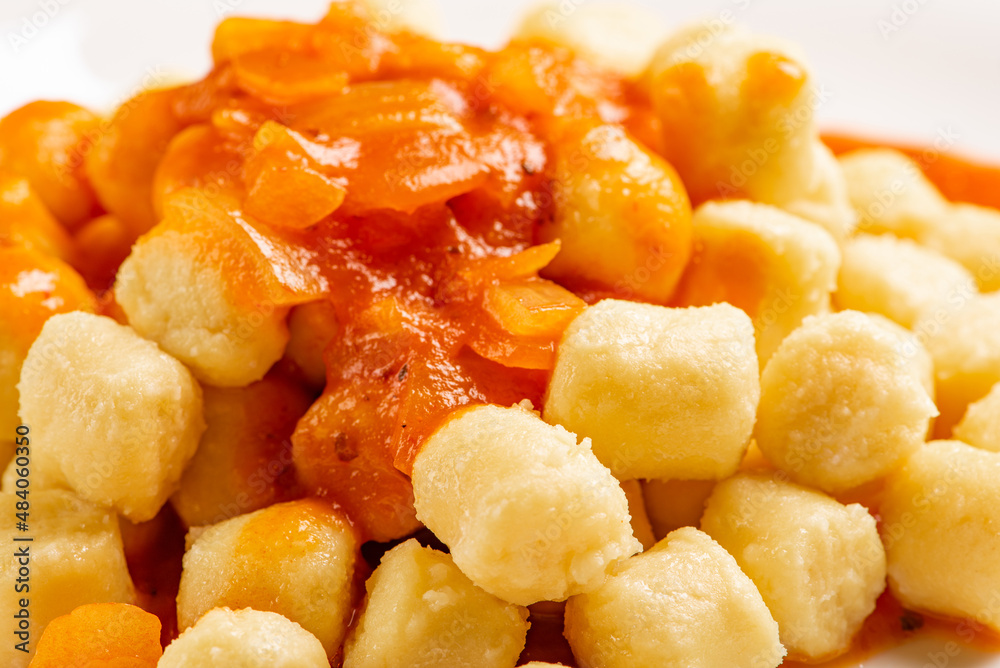 Potato gnocchi with sauce in detail on a white plate on a black and white checkered tablecloth, selective focus. Potato gnocchi with sauce in detail on a white plate on a black and white checkered tablecloth, selective focus.