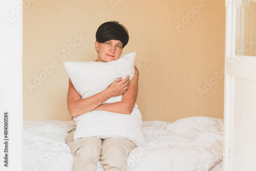 A middle-aged woman sits in bed hugging a pillow. Women's health depression sleep problems sadness loneliness.