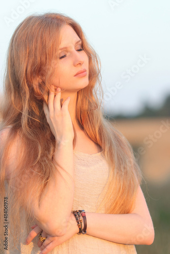 Beautiful Glamour Woman. Young pretty Woman with red hair at the field of wheat. Beauty Girl Outdoors enjoying Nature. Model girl with long healthy hair. Holidays, Travel, Summer, Trip, Lifestyle © Mariia