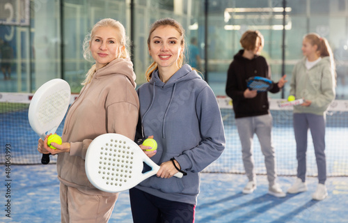Portrait of two athletic confident woman tennis players standing on the court with padel rackets and balls in their hands