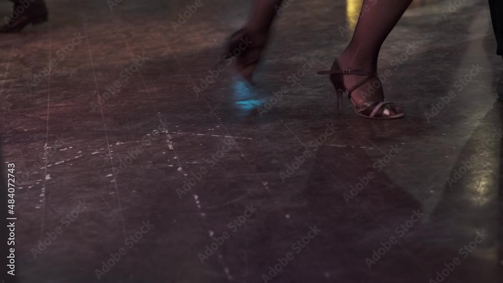 Close-up dancers legs performing tango in dark illuminated hall. Unrecognizable dance partners enjoy the movement on dark background. Milonga in vintage cafe. Close-up dancers legs performing tango in dark illuminated hall. Unrecognizable dance partners enjoy the movement on dark background. Milonga in vintage cafe.