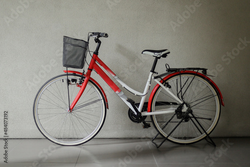 Red bicycle with basket in front of gray wall 